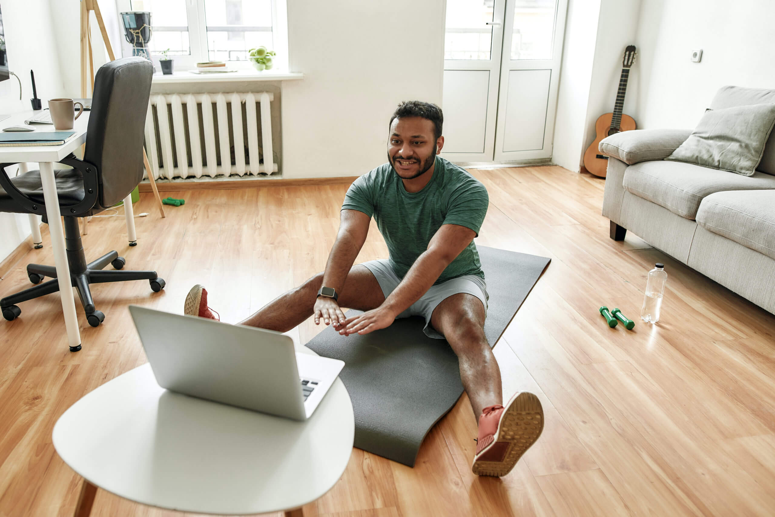 Cheerful stretching. Male fitness instructor showing exercises while streaming, broadcasting video lesson on training at home using laptop. Sport, online gym concept Cheerful stretching. Male fitness